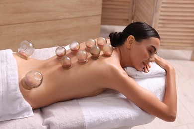 Photo of Cupping therapy. Woman with glass cups on massage couch in spa salon