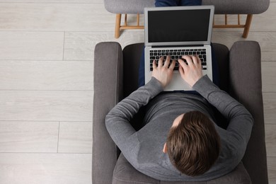 Photo of Man working with laptop in armchair, top view. Space for text