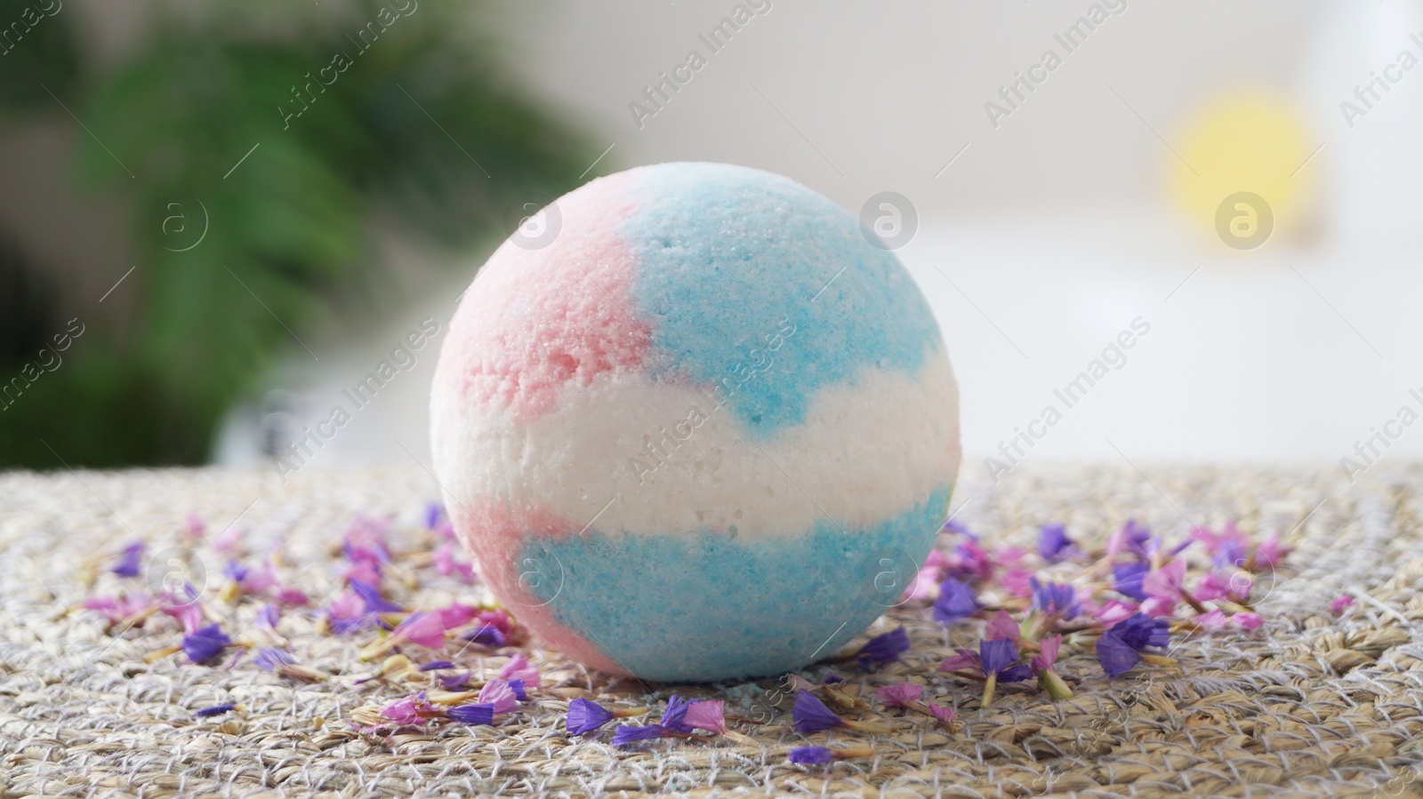 Photo of Beautiful bath bomb on wicker mat indoors, closeup