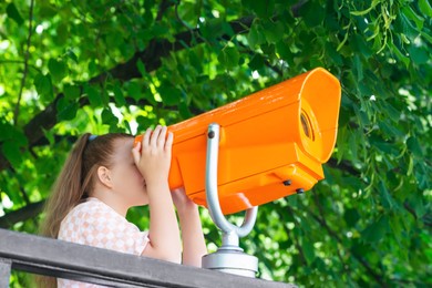 Girl looking through mounted binoculars outdoors on sunny day