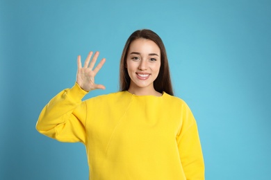 Woman showing number five with her hand on light blue background
