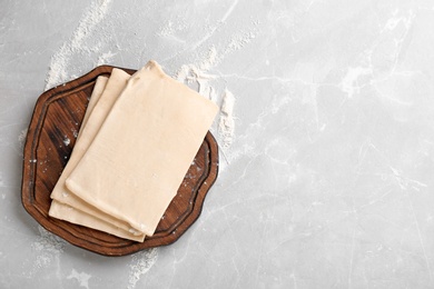 Photo of Wooden board with fresh dough on table, top view. Puff pastry