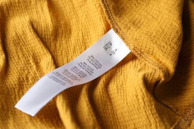 Photo of Clothing label with size and content information on yellow garment, closeup