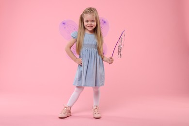 Cute little girl in fairy costume with violet wings and magic wand on pink background