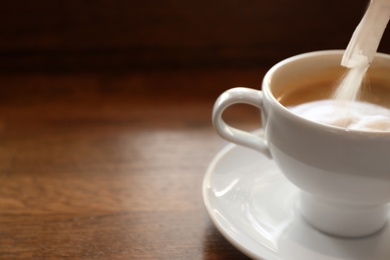 Adding sugar to fresh aromatic coffee on table, closeup