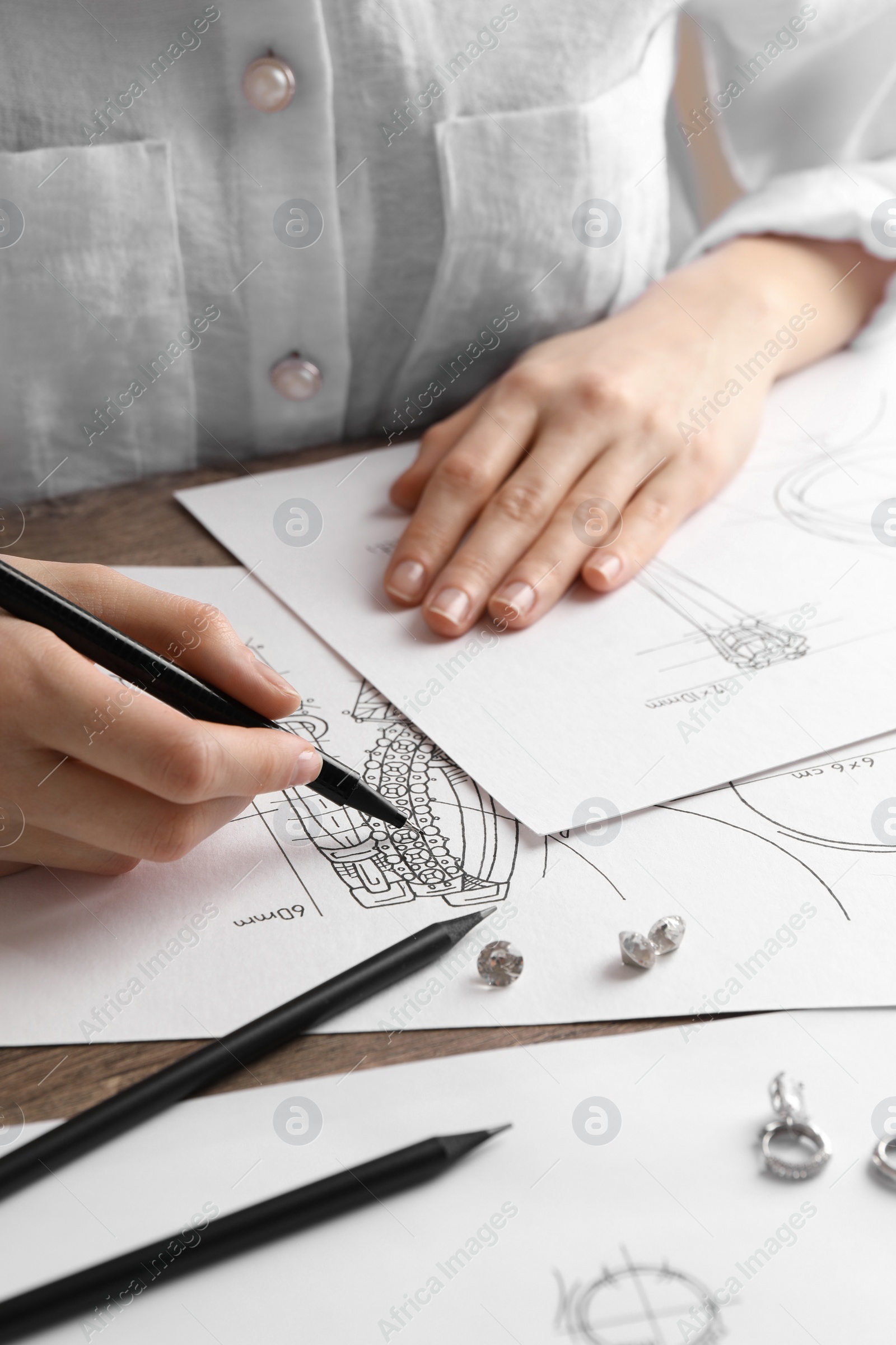 Photo of Jeweler drawing sketch of elegant earrings at wooden table, closeup