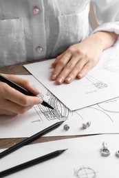 Photo of Jeweler drawing sketch of elegant earrings at wooden table, closeup