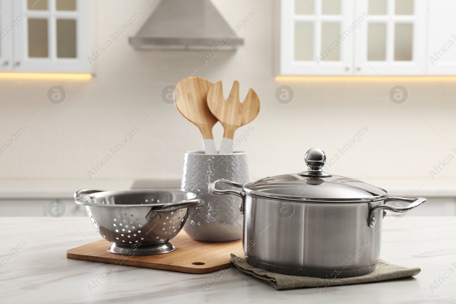 Photo of Pot, colander and kitchen utensils on white table indoors