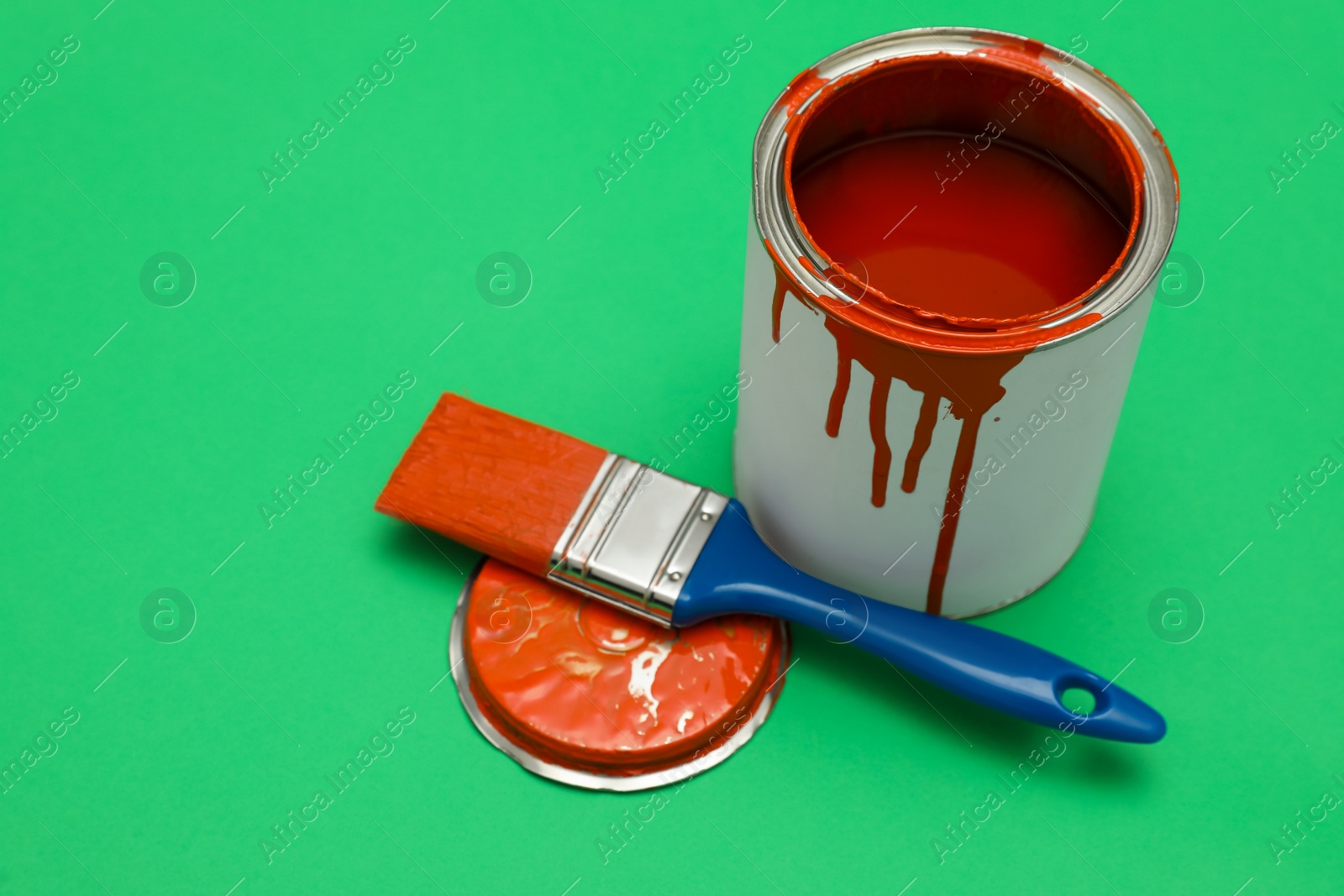 Photo of Can of orange paint and brush on green background. Space for text