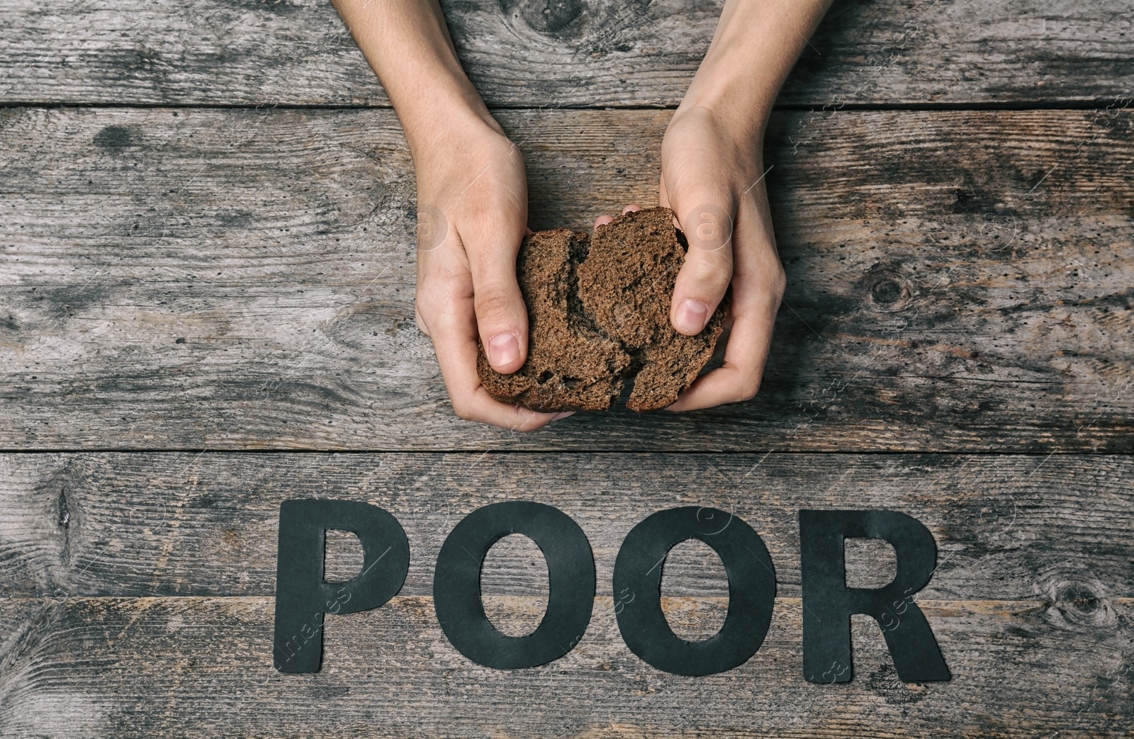 Photo of Poor woman holding piece of rye bread over wooden background, top view