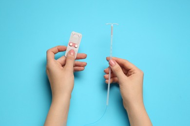 Photo of Woman with contraceptive pills and intrauterine device on light blue background, top view. Choosing birth control method