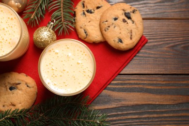 Photo of Tasty eggnog, cookies, baubles and fir branches on wooden table, flat lay. Space for text