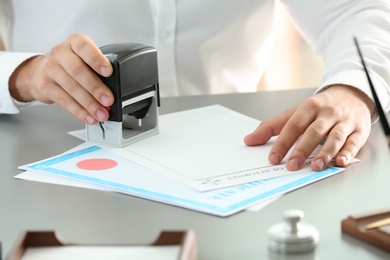 Male notary stamping document at table, closeup