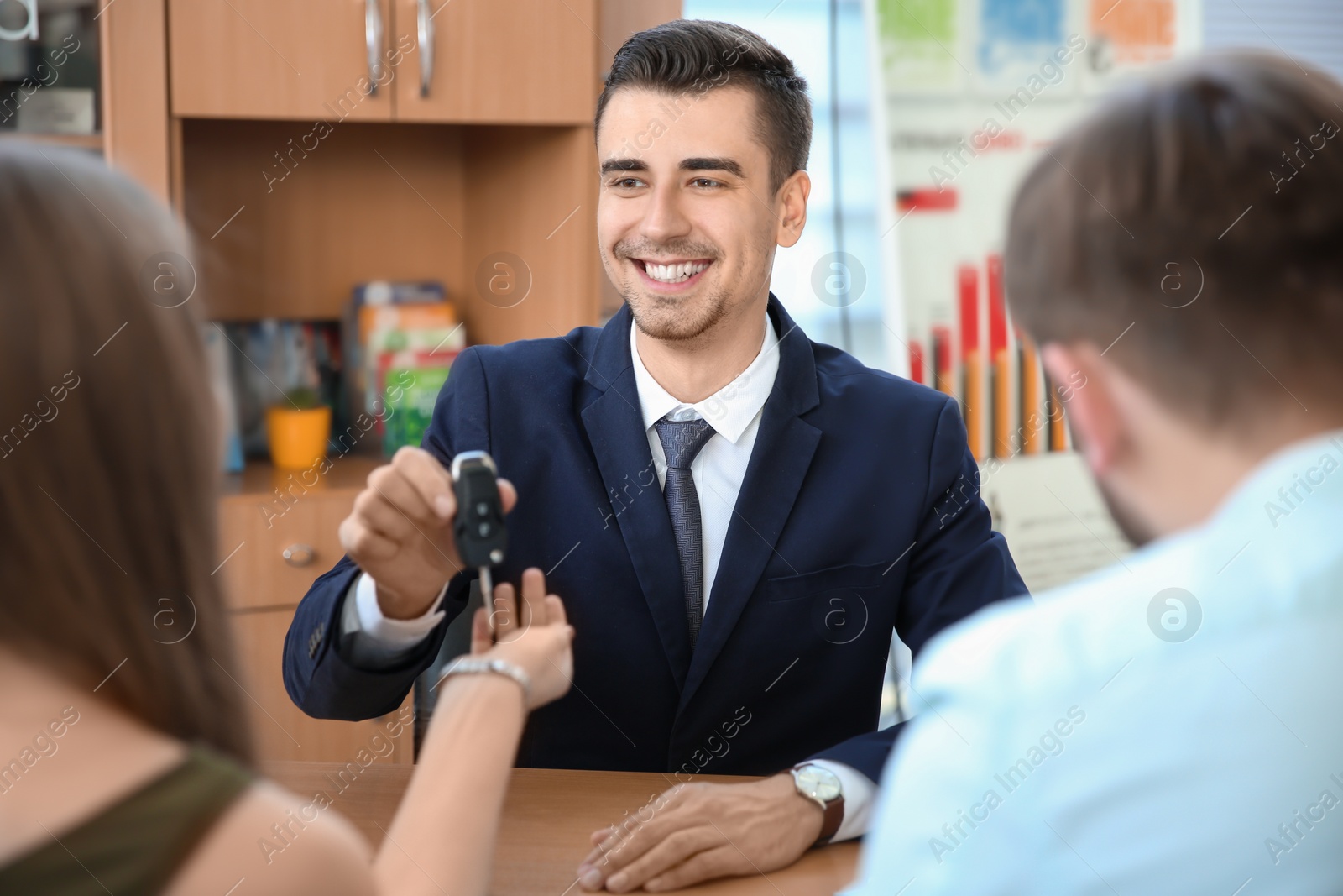 Photo of Salesman giving car key to young couple in salon