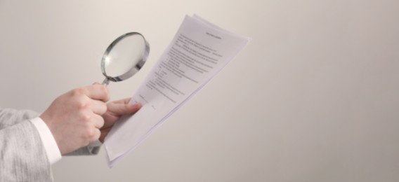 Man looking at documents through magnifier on light background, closeup. Banner design with space for text