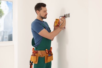 Electrician in uniform with tester checking voltage indoors