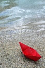 Beautiful red paper boat on sandy beach near water outdoors