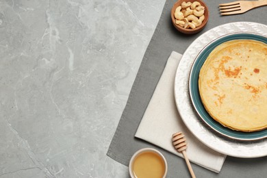 Delicious crepes, pine nuts and honey on light grey table, flat lay. Space for text