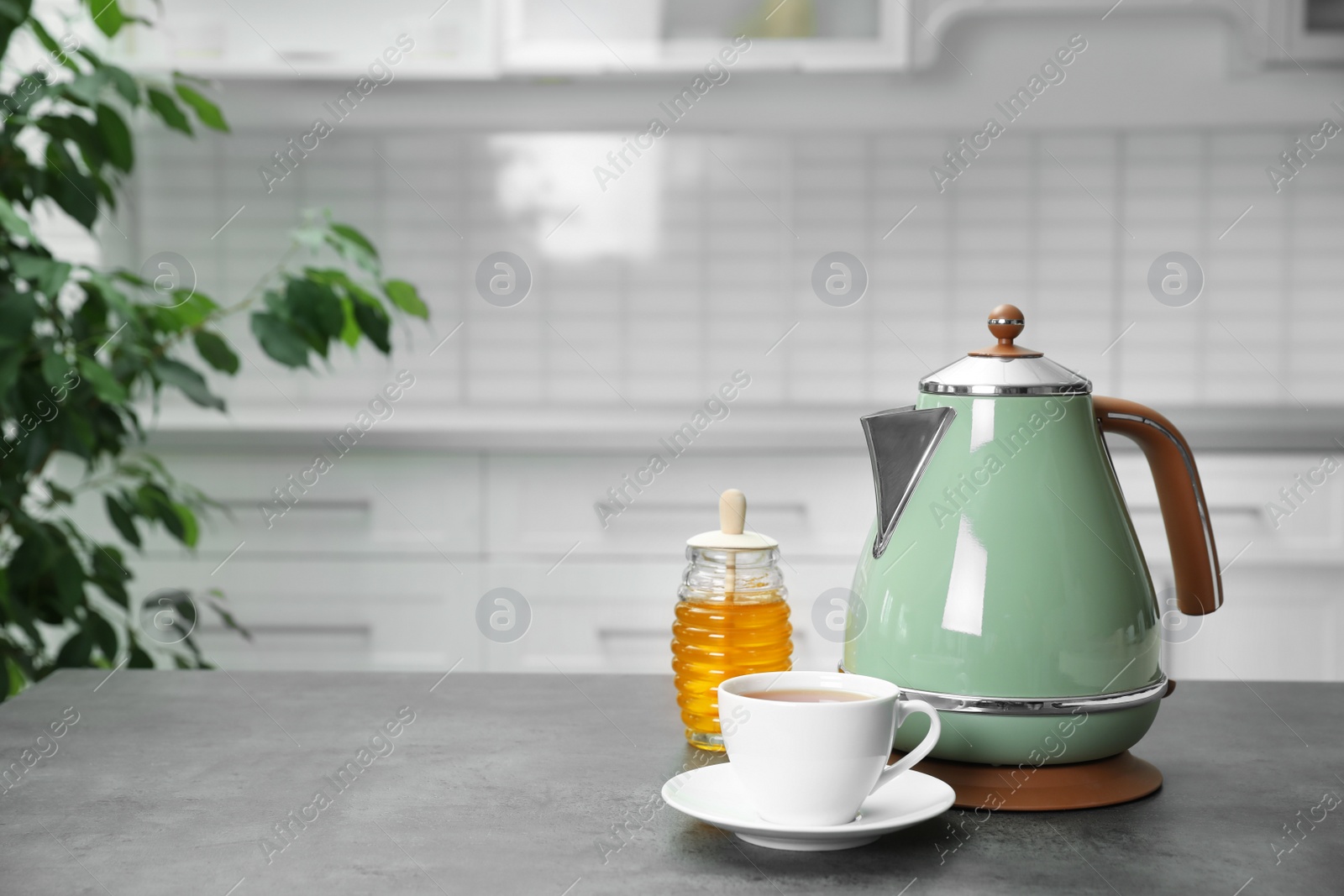 Photo of Modern electric kettle, cup of tea and honey on grey table in kitchen