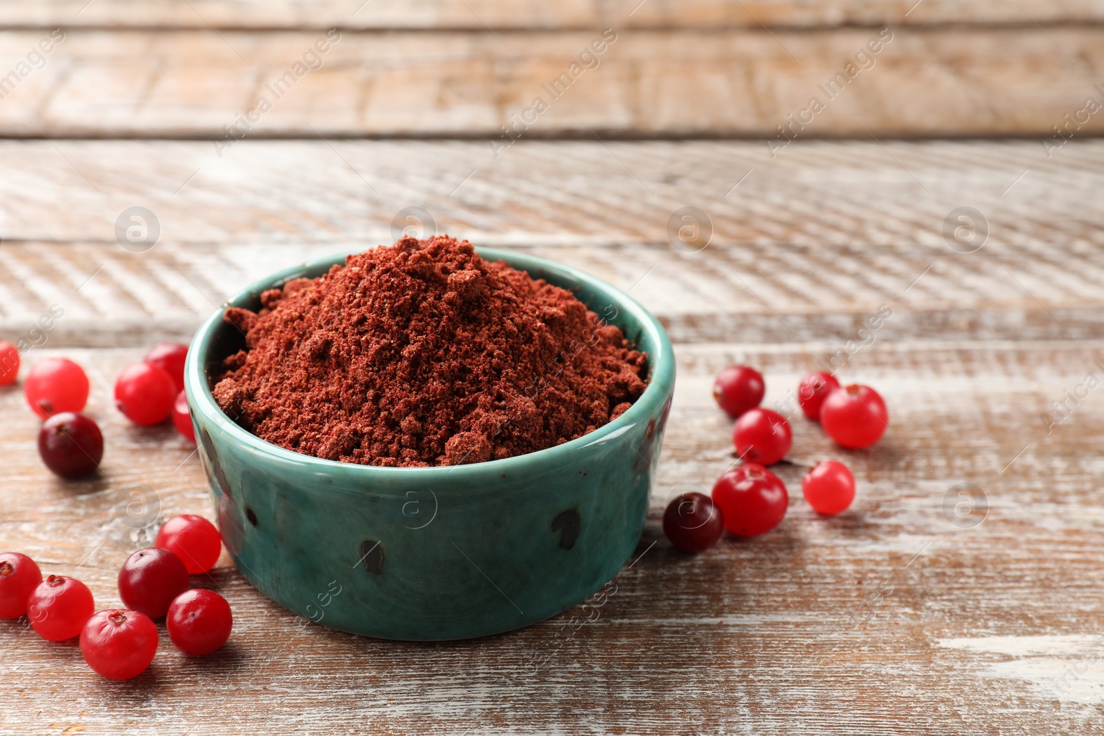 Photo of Cranberry powder in bowl and fresh berries on wooden table, closeup. Space for text