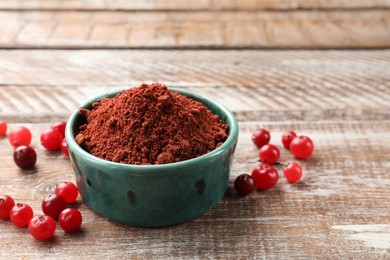 Photo of Cranberry powder in bowl and fresh berries on wooden table, closeup. Space for text