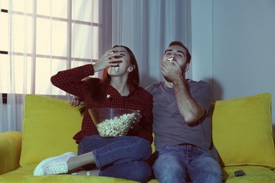 Photo of Happy young couple eating popcorn while watching TV on sofa at home