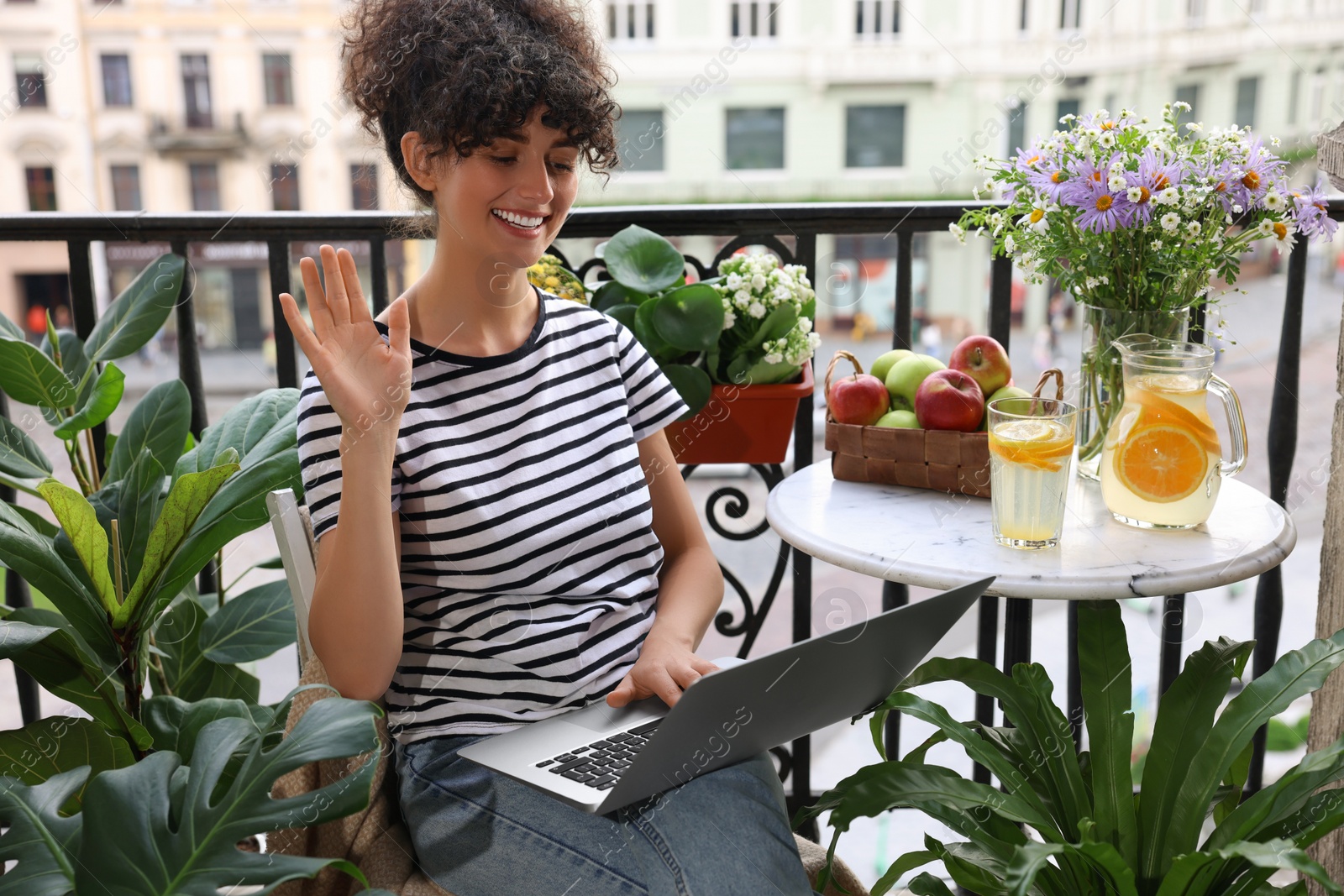 Photo of Beautiful young woman using laptop on balcony with green houseplants