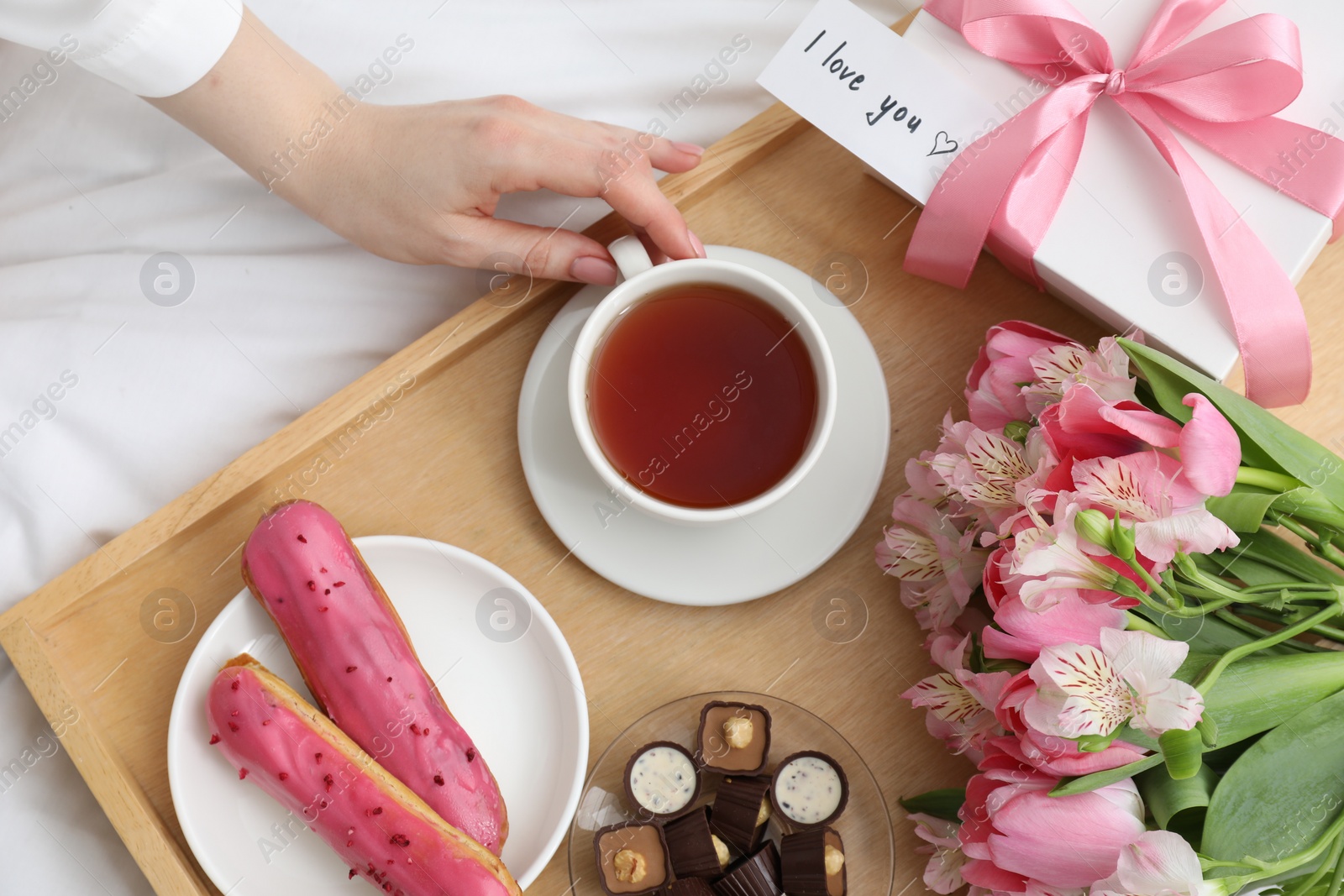 Photo of Tasty breakfast served in bed. Woman with tea, desserts, gift box, flowers and I Love You card at home, top view