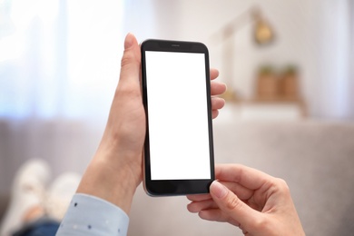 Woman holding smartphone with blank screen indoors, closeup of hands. Space for text