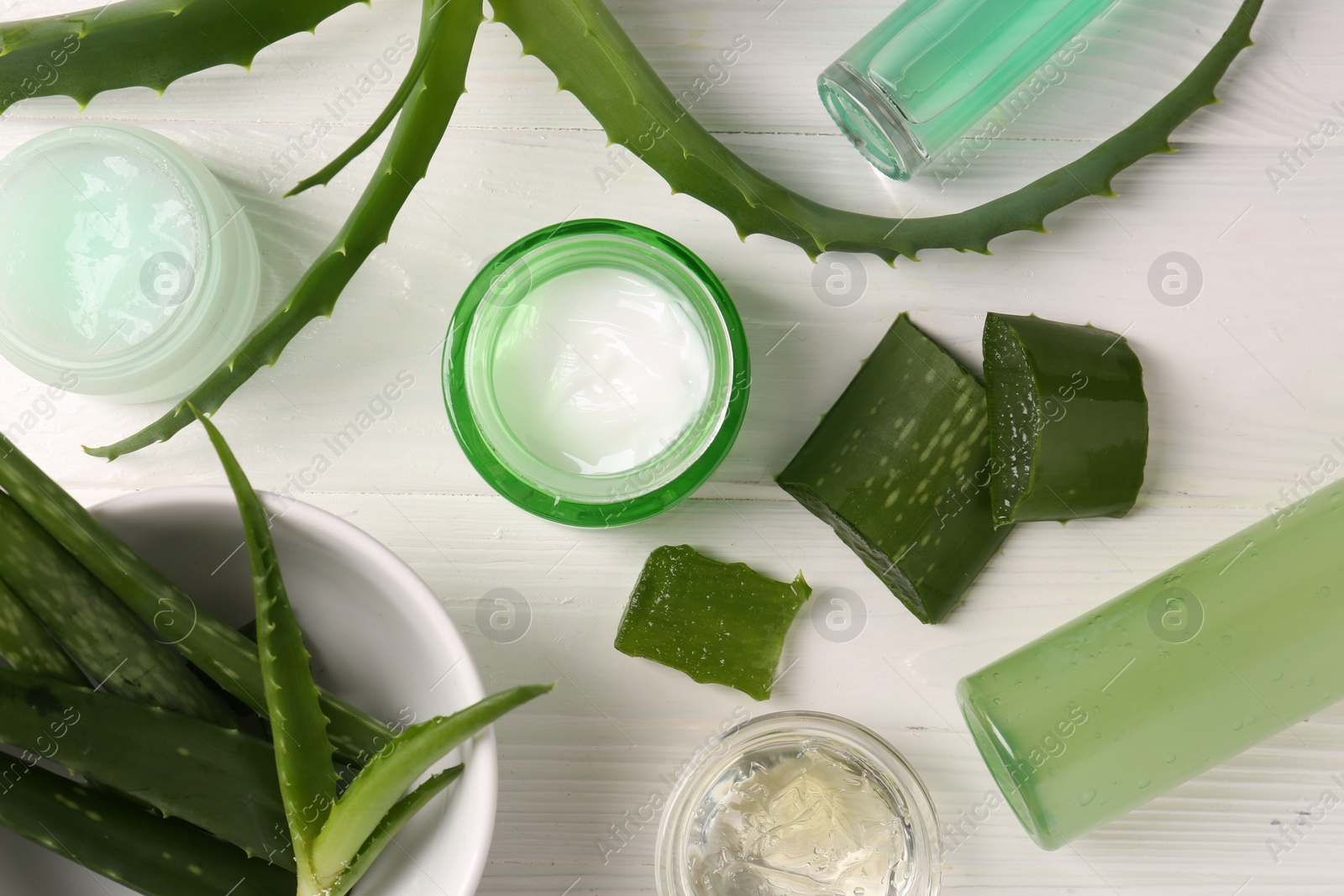 Photo of Different cosmetic products and cut aloe vera leaves on white wooden table, flat lay
