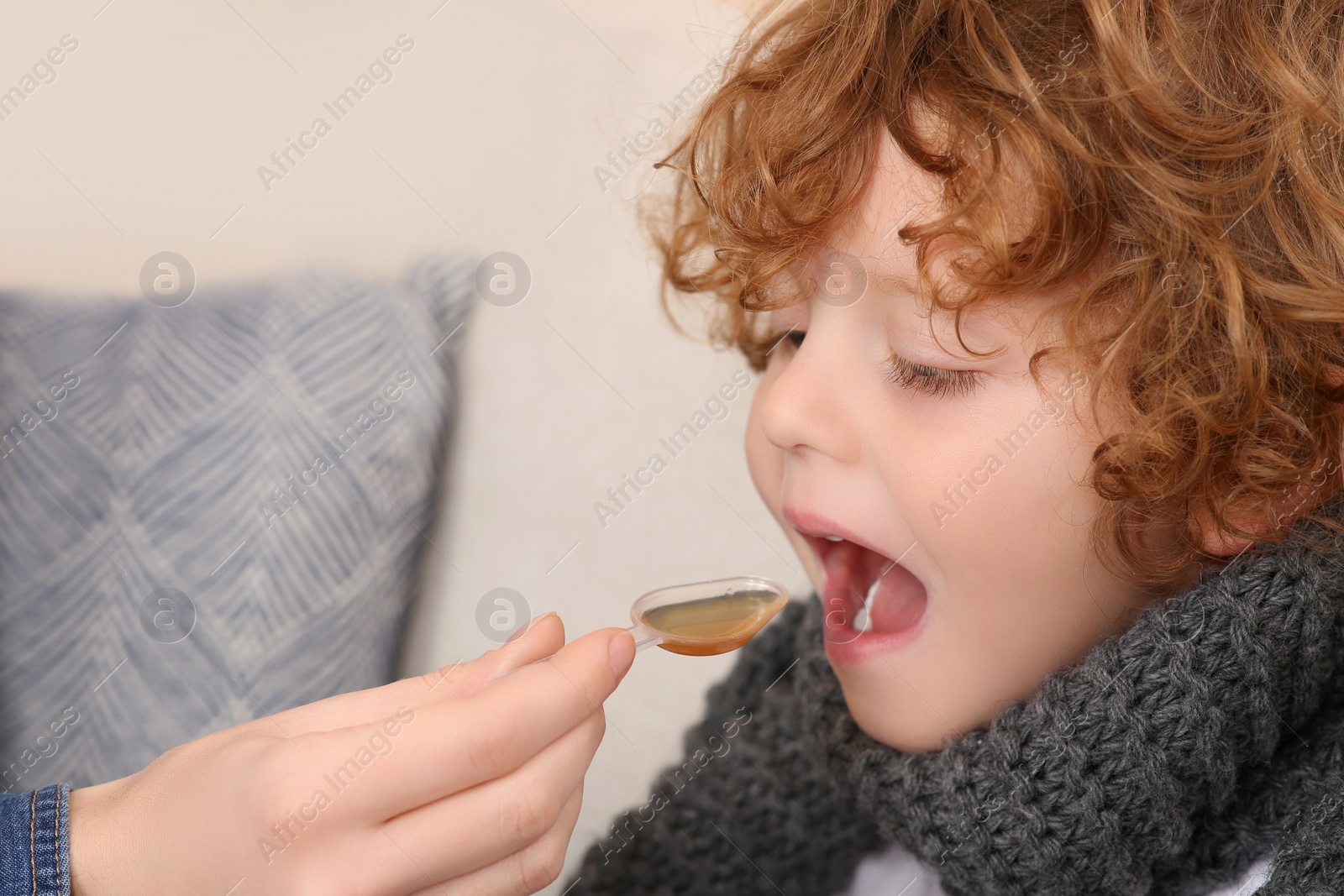 Photo of Mother giving cough syrup to her son on sofa