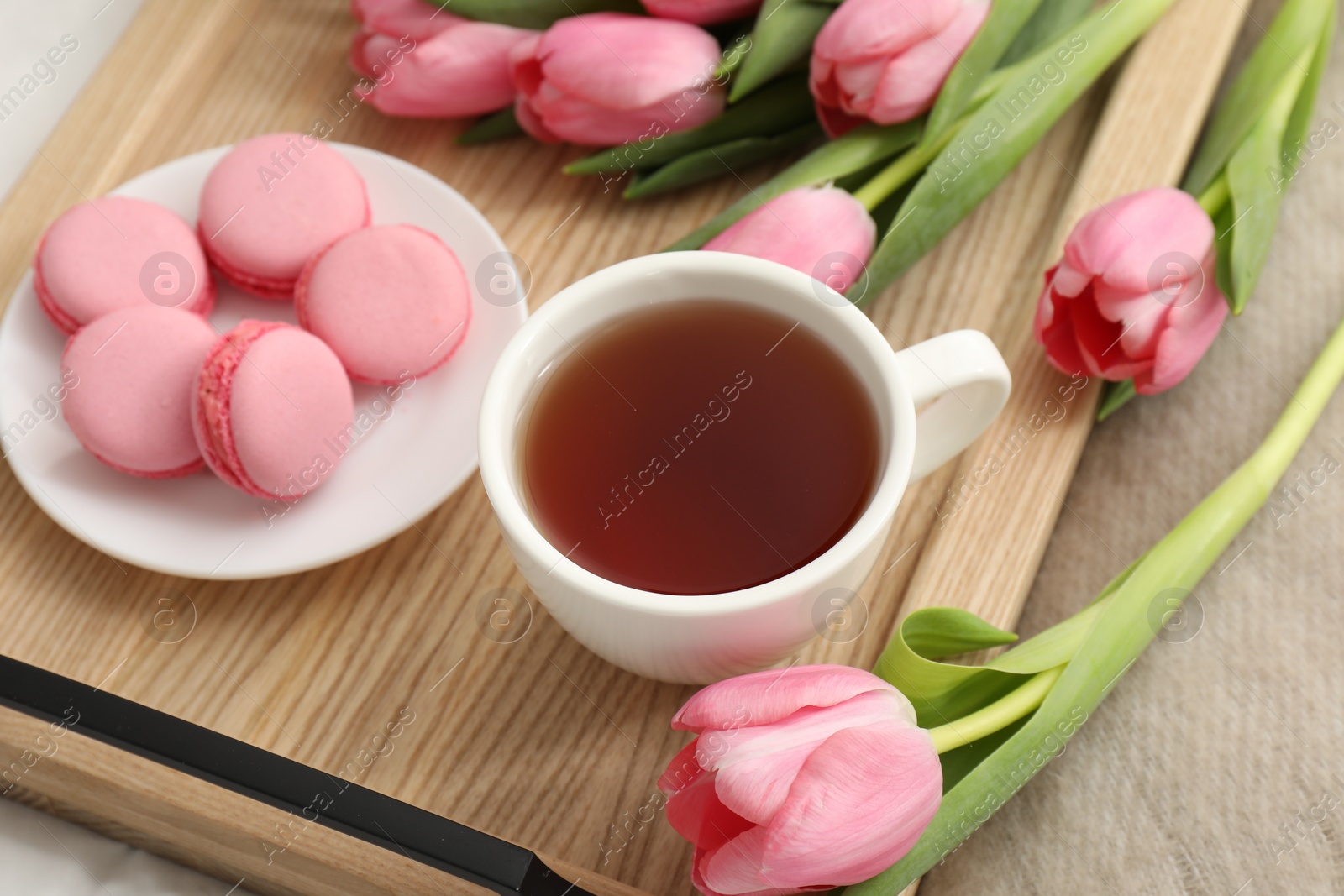 Photo of Tasty breakfast served in bed. Delicious macarons, tea and flowers on tray, closeup