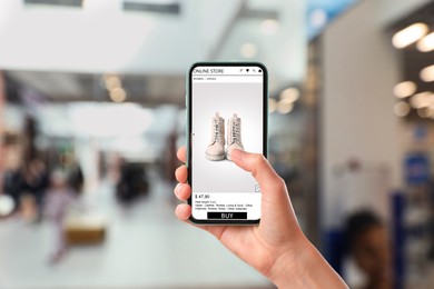 Image of Woman visiting shop to take ordered boots indoors, closeup. Online store website on device screen