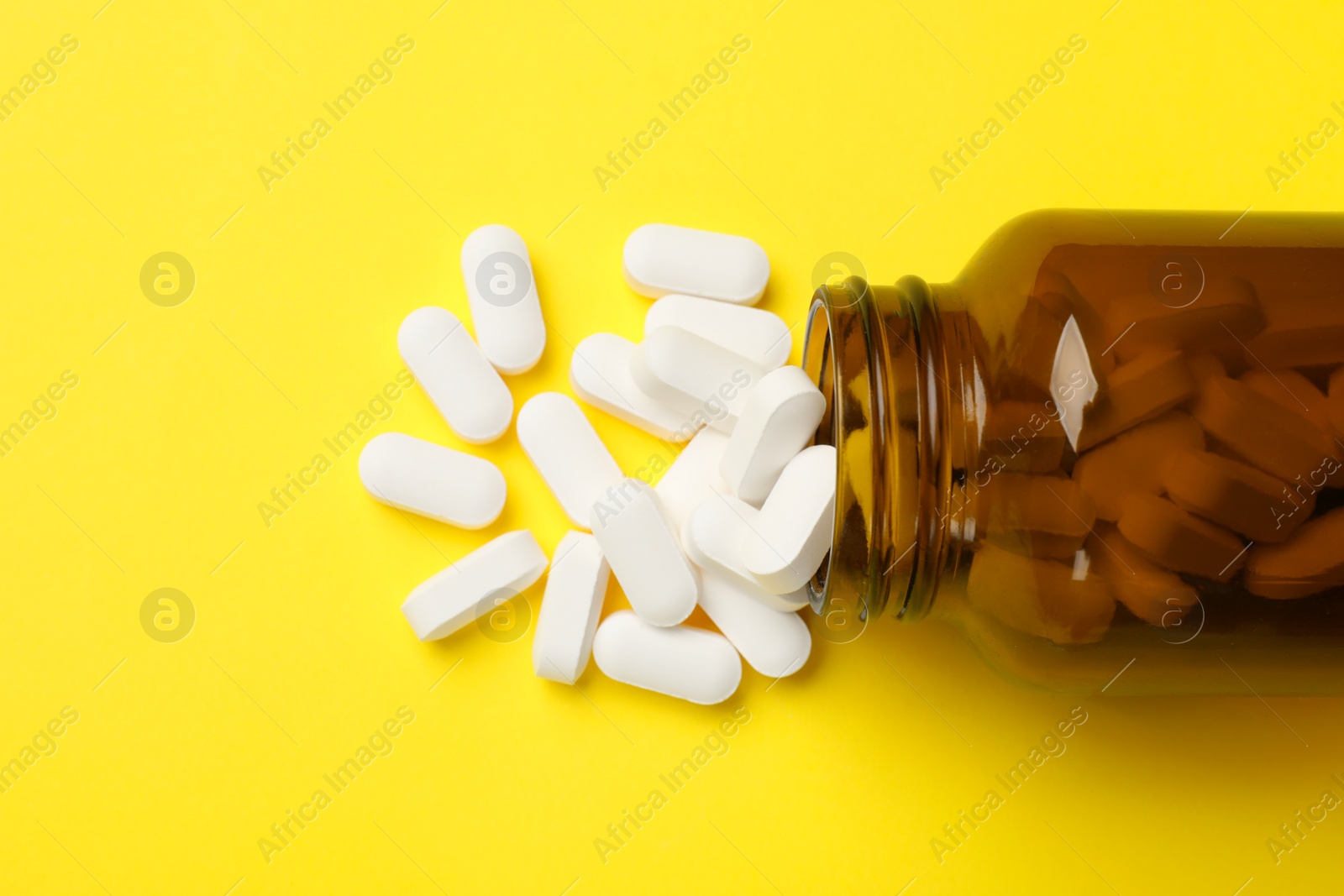 Photo of Vitamin pills and bottle on yellow background, top view