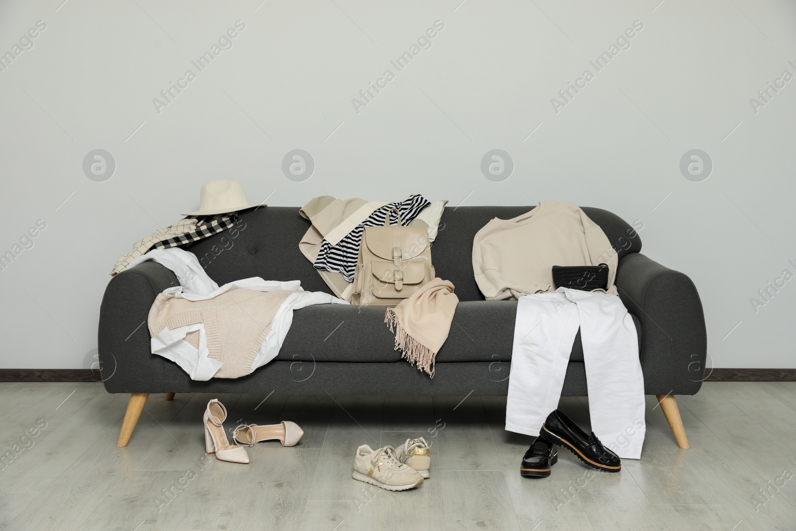 Photo of Messy pile of clothes on sofa and shoes in living room