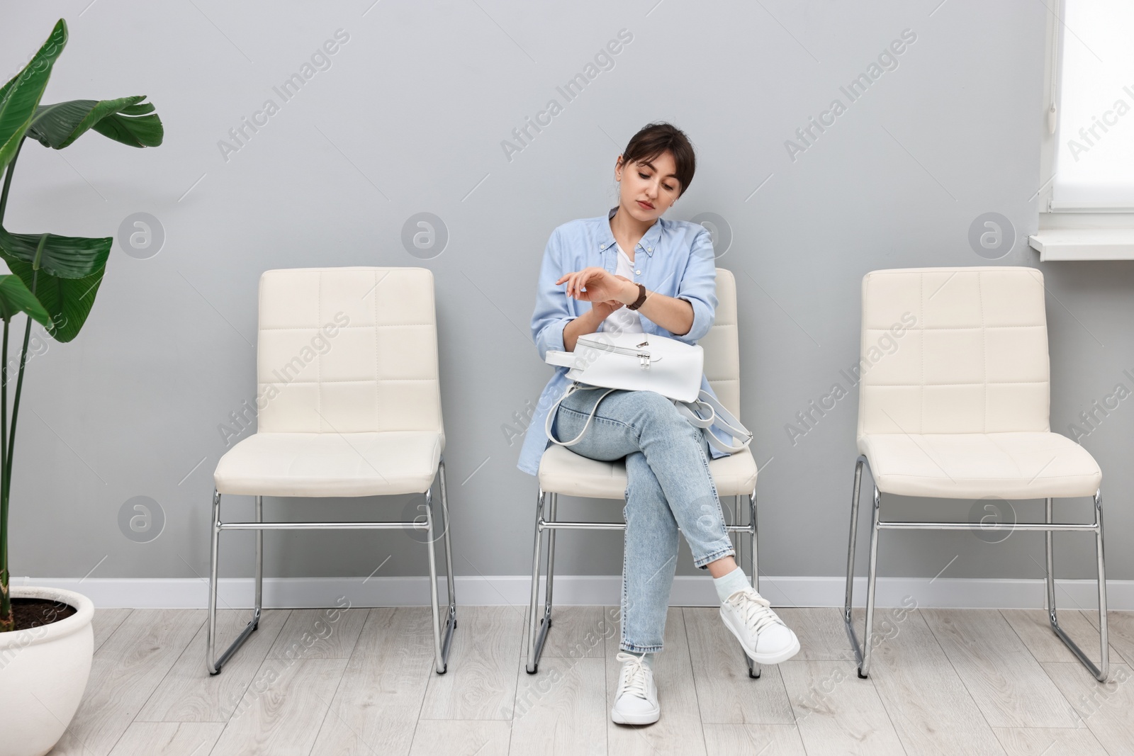 Photo of Woman looking at wrist watch and waiting for appointment indoors