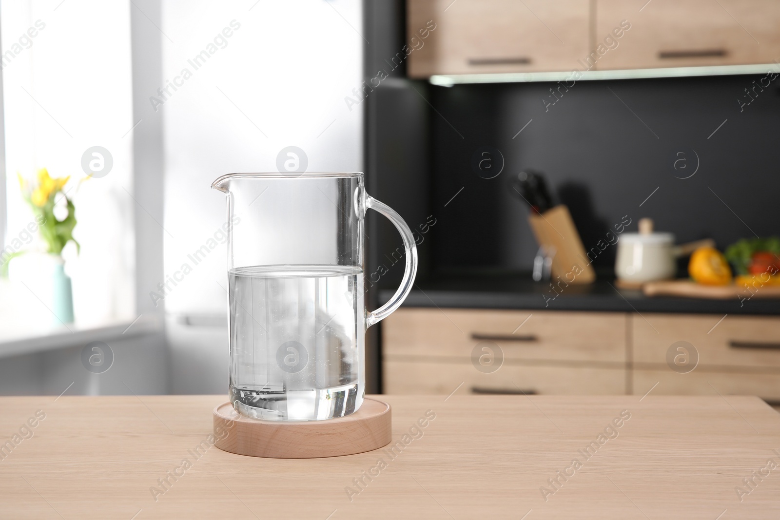 Photo of Glass jug with water on wooden table in kitchen