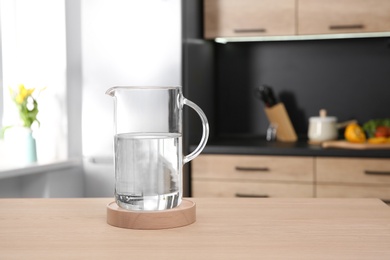 Photo of Glass jug with water on wooden table in kitchen
