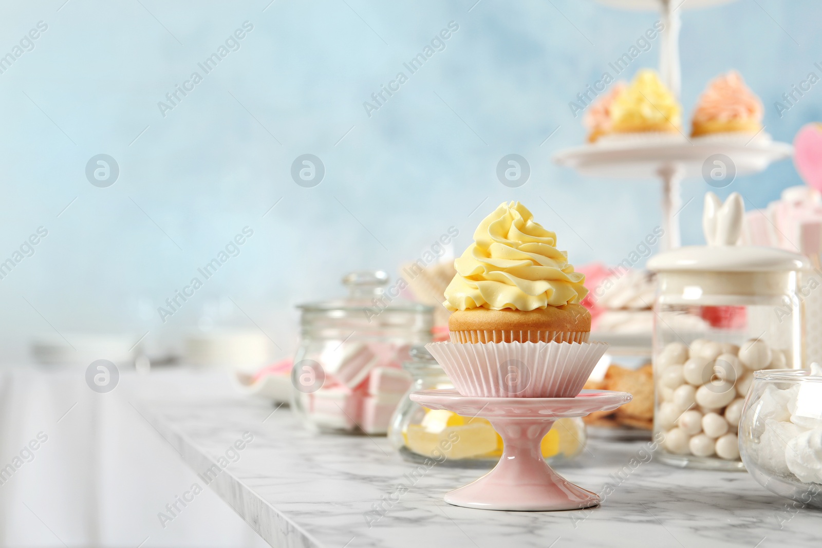 Photo of Stand with cupcake and other sweets on white marble table, space for text. Candy bar