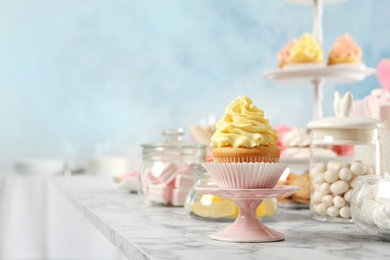 Stand with cupcake and other sweets on white marble table, space for text. Candy bar