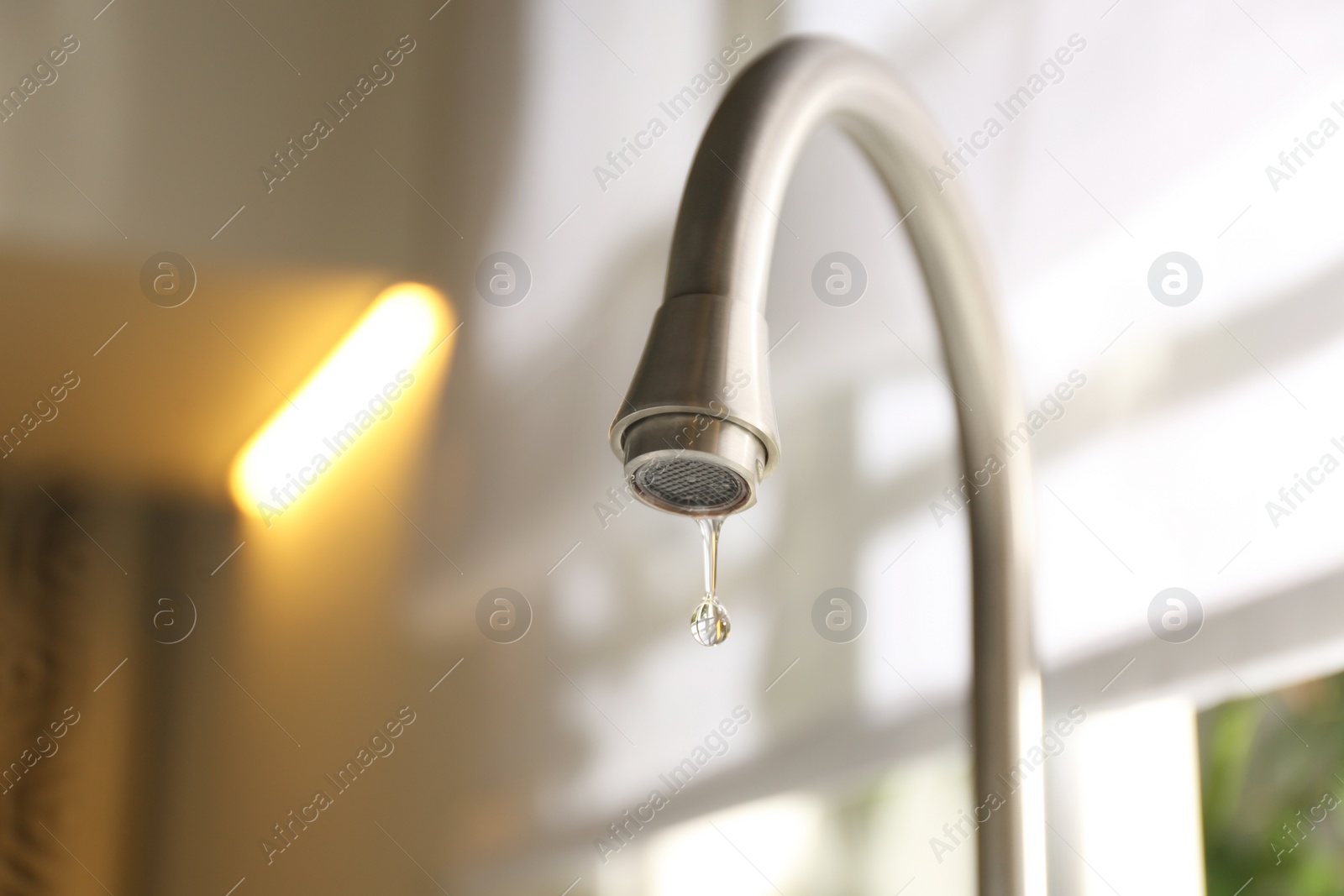 Photo of Water drop falling down from tap on blurred background, closeup