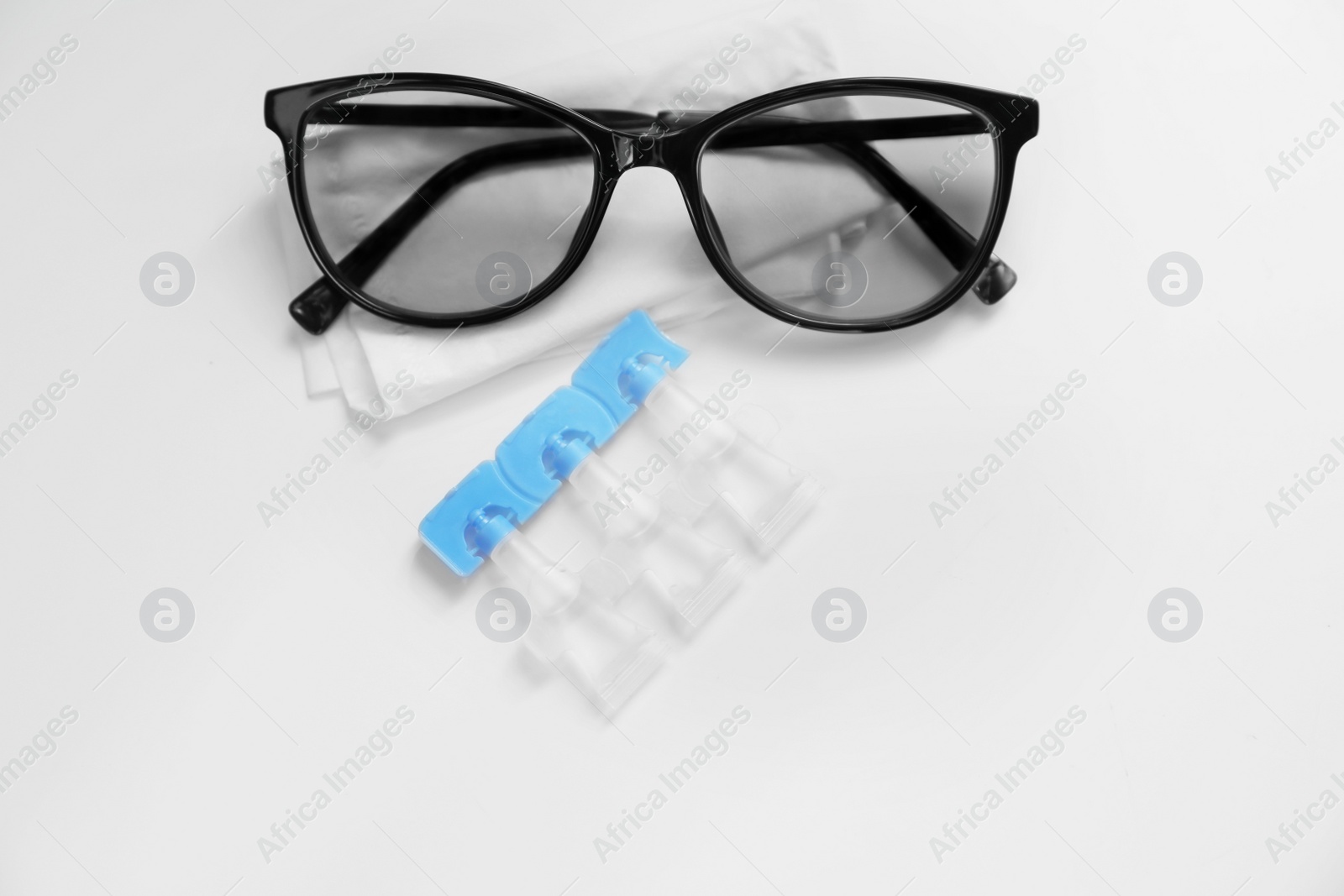 Photo of Single dose eye drops, glasses and fabric on white table, above view