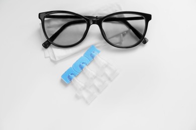 Single dose eye drops, glasses and fabric on white table, above view