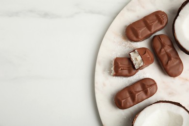 Photo of Delicious milk chocolate candy bars with coconut filling on white table, flat lay. Space for text