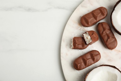 Delicious milk chocolate candy bars with coconut filling on white table, flat lay. Space for text