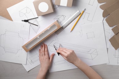 Photo of Woman creating packaging design at light wooden table, top view