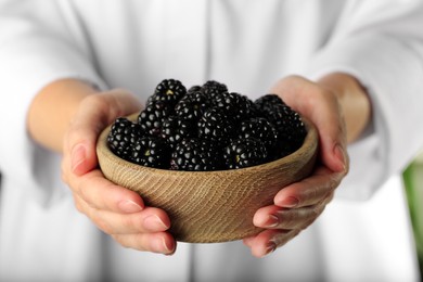 Photo of Woman holding bowl of fresh ripe black blackberries, closeup