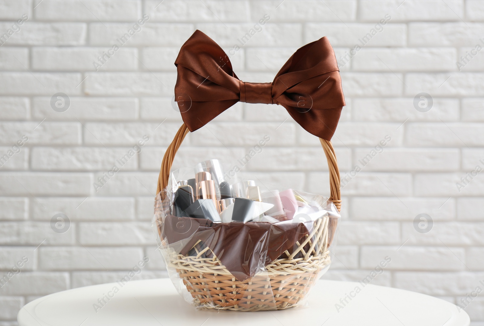 Photo of Wicker gift basket with cosmetic products on table near white brick wall