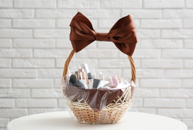 Wicker gift basket with cosmetic products on table near white brick wall