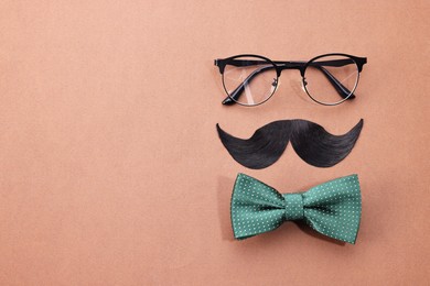 Photo of Man's face made of artificial mustache, glasses and bow tie on brown background, top view. Space for text